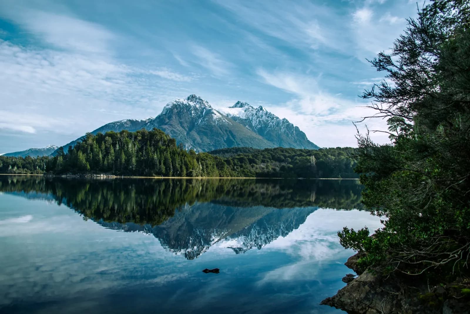 A snow-capped peak mirrored in a still lake ringed by alpine forest in the Bariloche Lake District