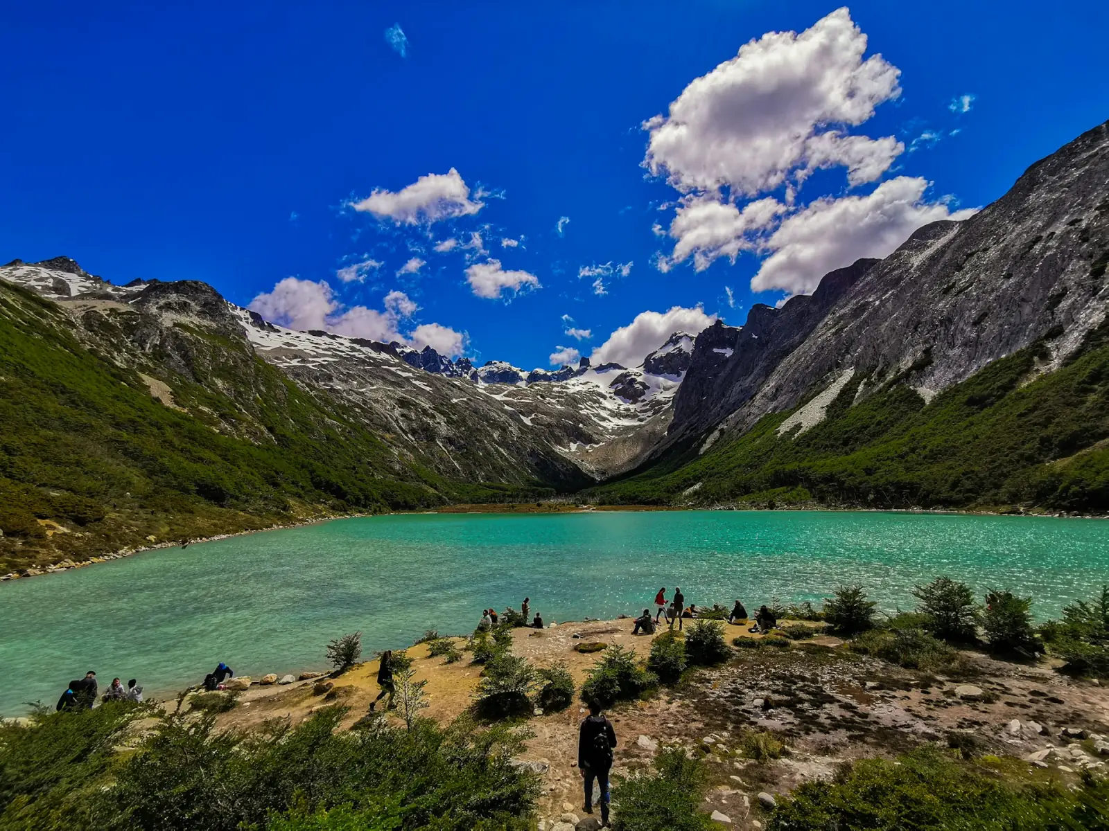 Hikers beside the turquoise Laguna Esmeralda ringed by snow-streaked peaks in Tierra del Fuego
