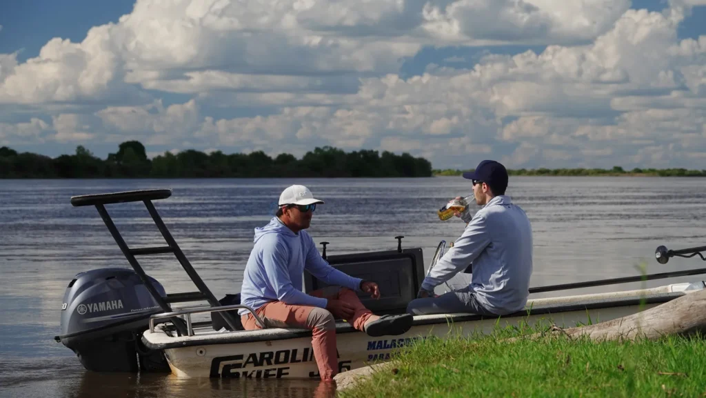 Two anglers relaxing and having a drink on a fishing skiff boat on the river bank