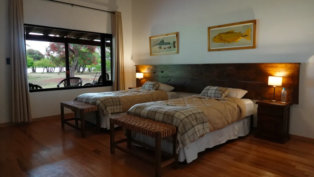 Comfortable twin bedroom in the fishing lodge with rustic wooden furniture and view of the gardens