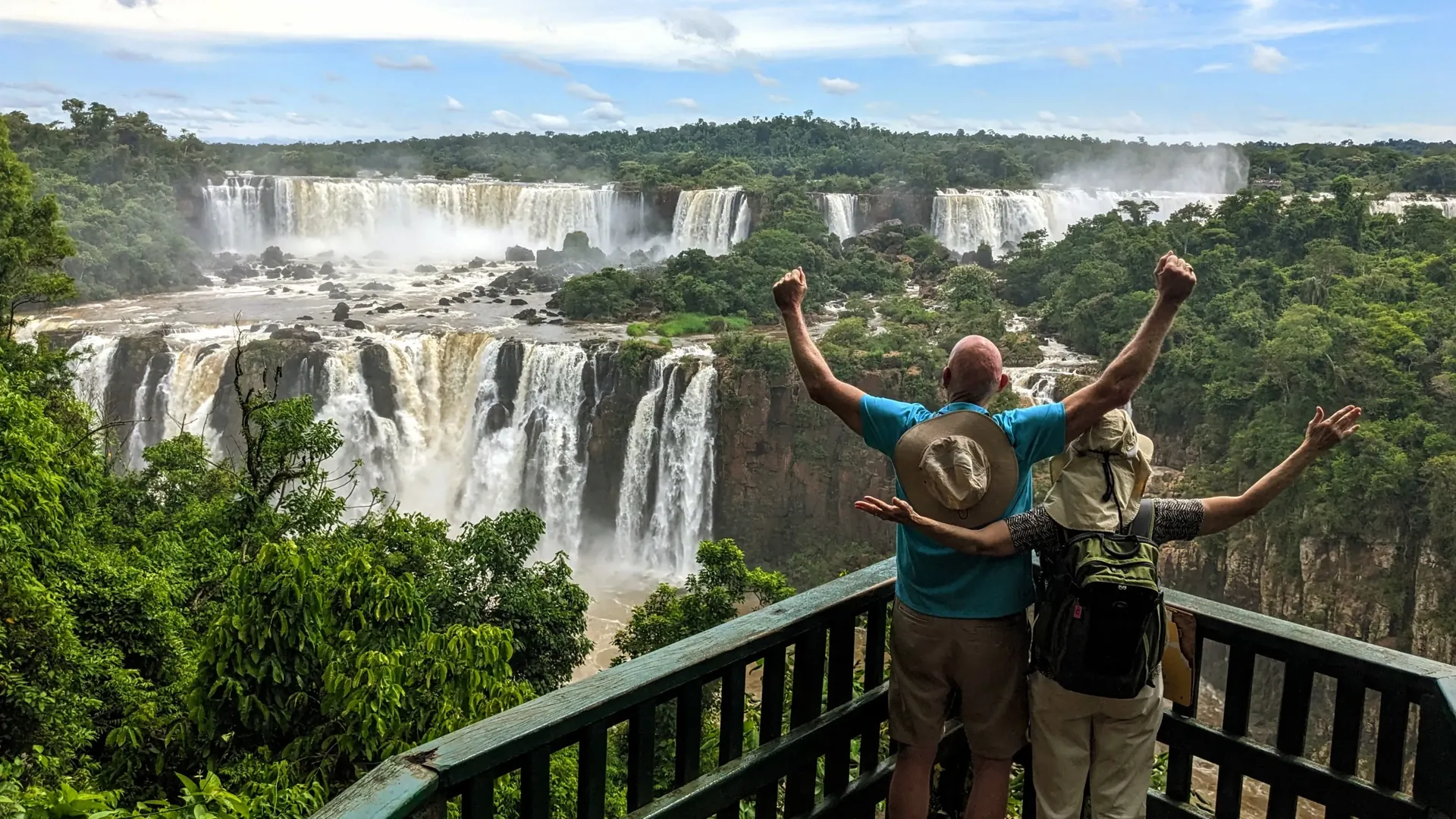 A couple raising their arms in joy while admiring the panoramic view of Iguazu Falls