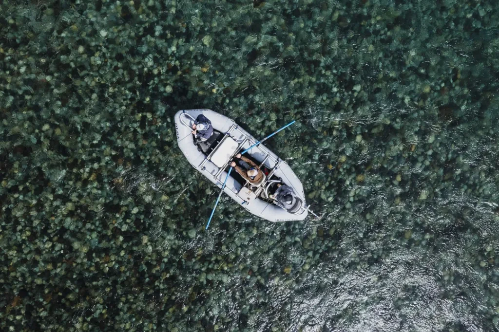 Aerial top-down view of a drift boat navigating the crystal clear waters of a Patagonia river surrounded by lush vegetation