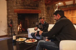 Two friends toasting with red wine in front of a warm fireplace at the fishing lodge