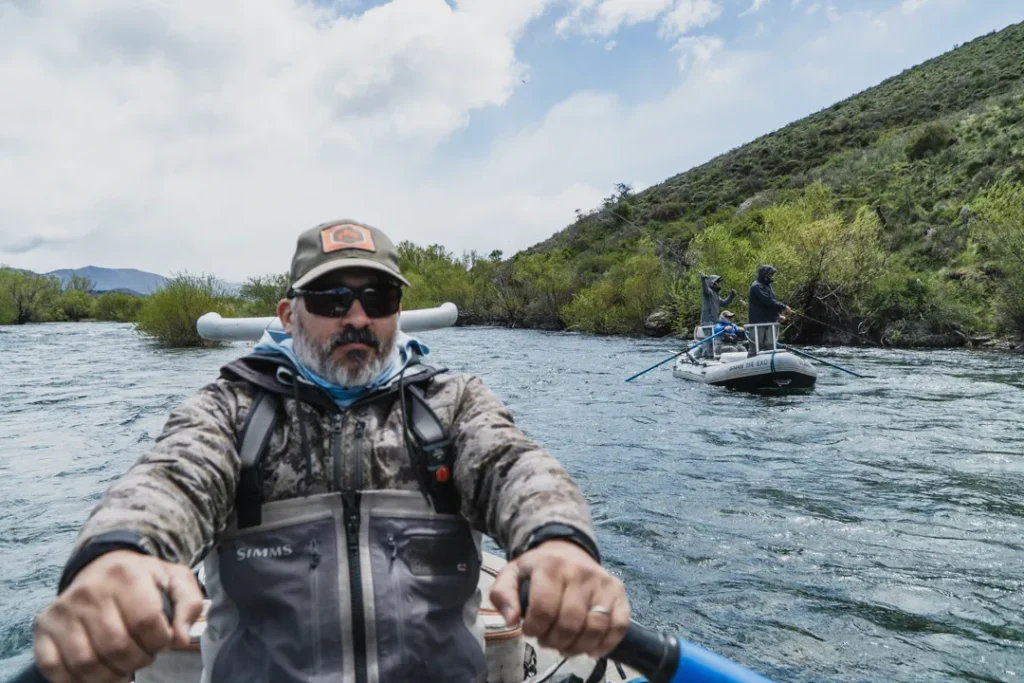 Fishing guide rowing a drift boat on a Patagonia river with angler in the background