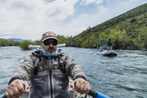 Fishing guide rowing a drift boat on a Patagonia river with angler in the background
