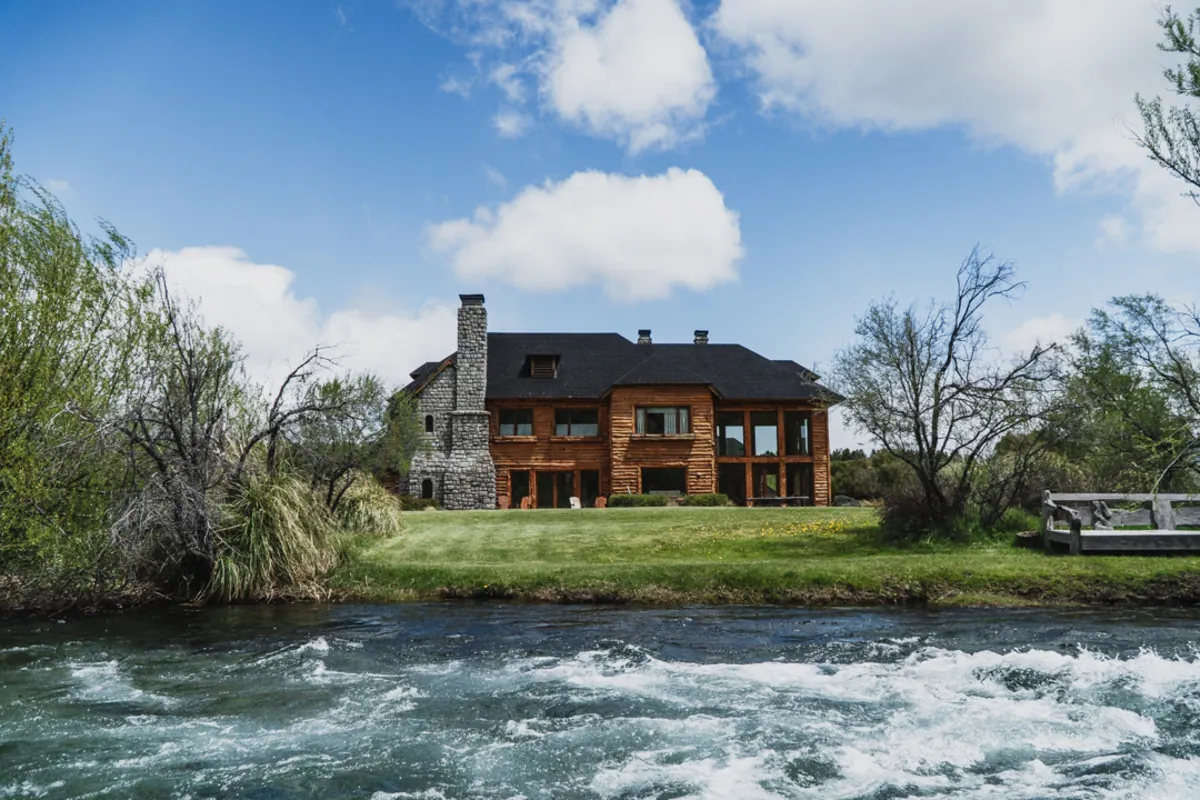 View of the grand timber and stone fishing lodge from across the flowing river