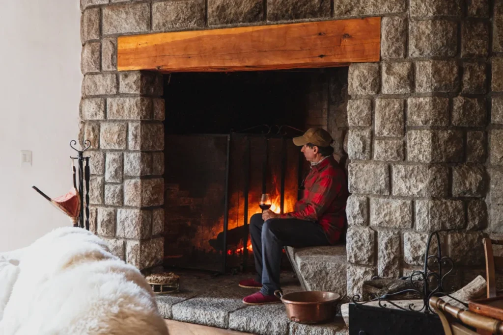 Angler relaxing by a large stone fireplace with a glass of wine in a luxury Patagonia fishing lodge