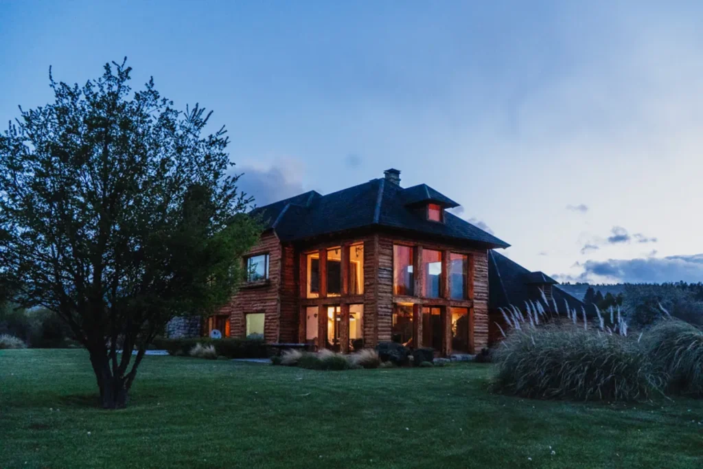 Exterior view of a rustic log cabin fishing lodge illuminated at twilight in Patagonia