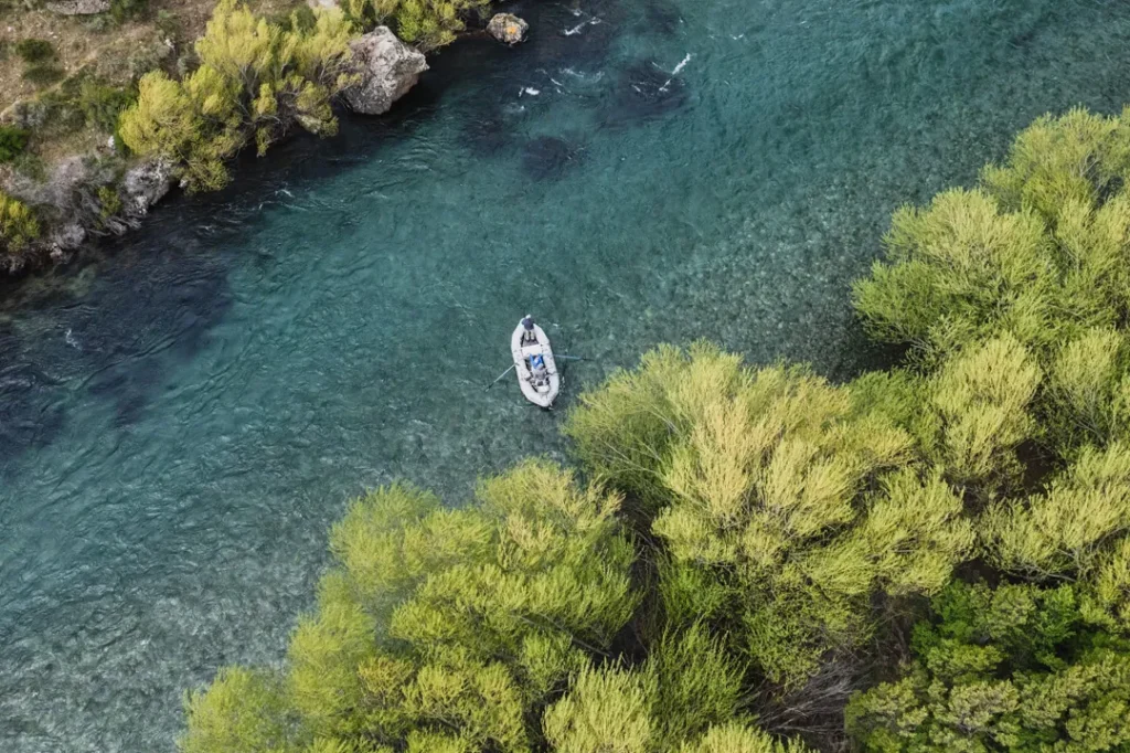 Aerial view of a drift boat fishing on a scenic Patagonia river bordered by vibrant green trees